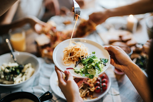 Group of joyful people passing and sharing food across table
