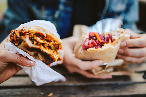 Close up image of two people eating a Texas style pulled pork barbeque and a falafel fast food in East London